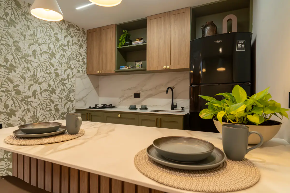 Cocina compartida con gabinetes de madera, nevera, estufa, papel de colgadura botánico y un mesón con vajilla gris.