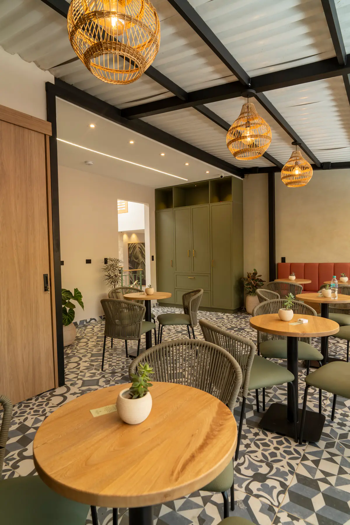 Zona de coworking con mesas redondas de madera, sillas tejidas, piso de baldosa estampada y lámparas tejidas.