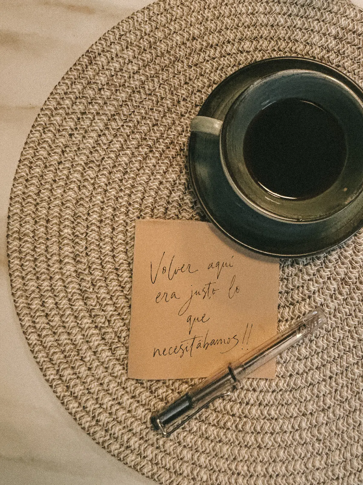 Una taza de café sobre un individual tejido y una nota a mano: «Volver aquí era justo lo que necesitábamos!!».
