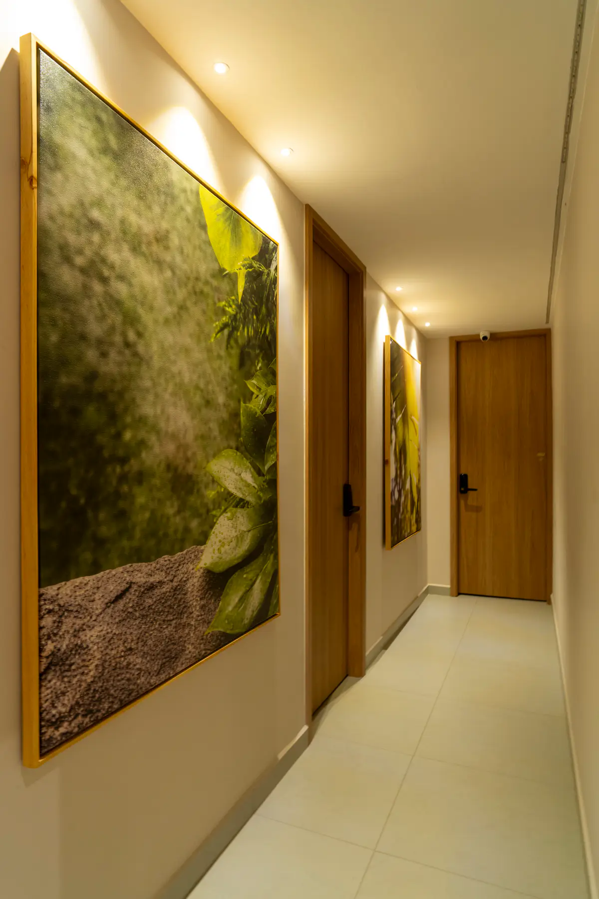 Pasillo con luz cálida, un cuadro de musgo y follaje en la pared y puertas de madera.
